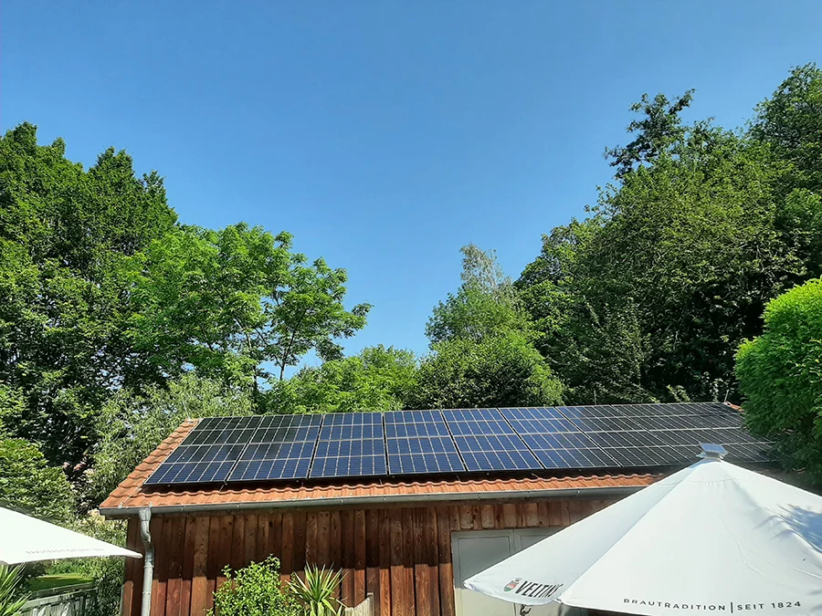 Solaranlage auf Holzdach bei sonnigem Wetter und blauem Himmel, umgeben von grünen Bäumen